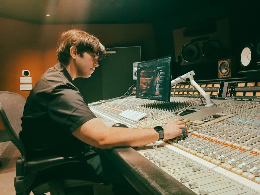 Dax at a large studio mixing console with monitors and speakers behind it